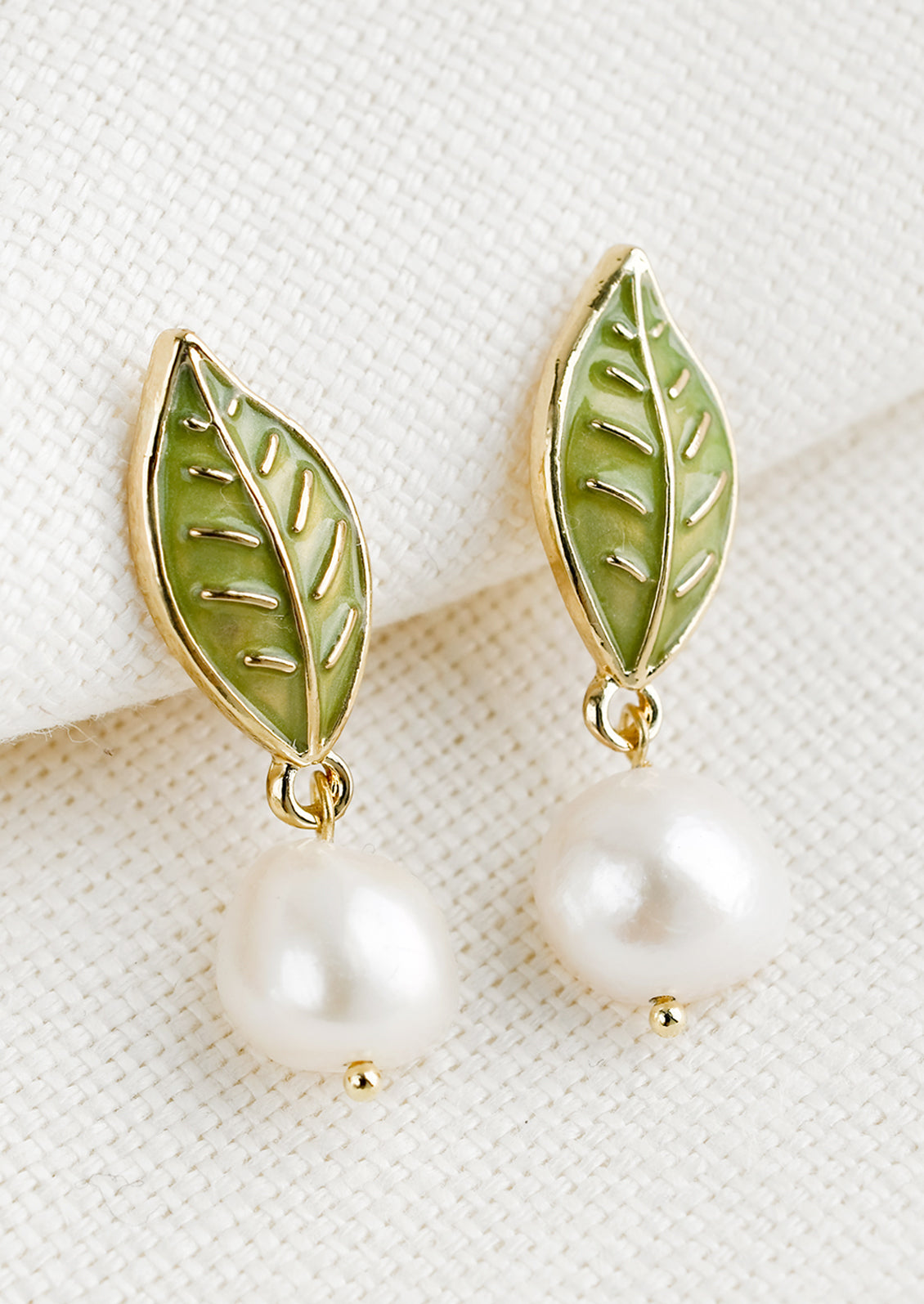 A pair of earrings with leaf enamel post and pearl.
