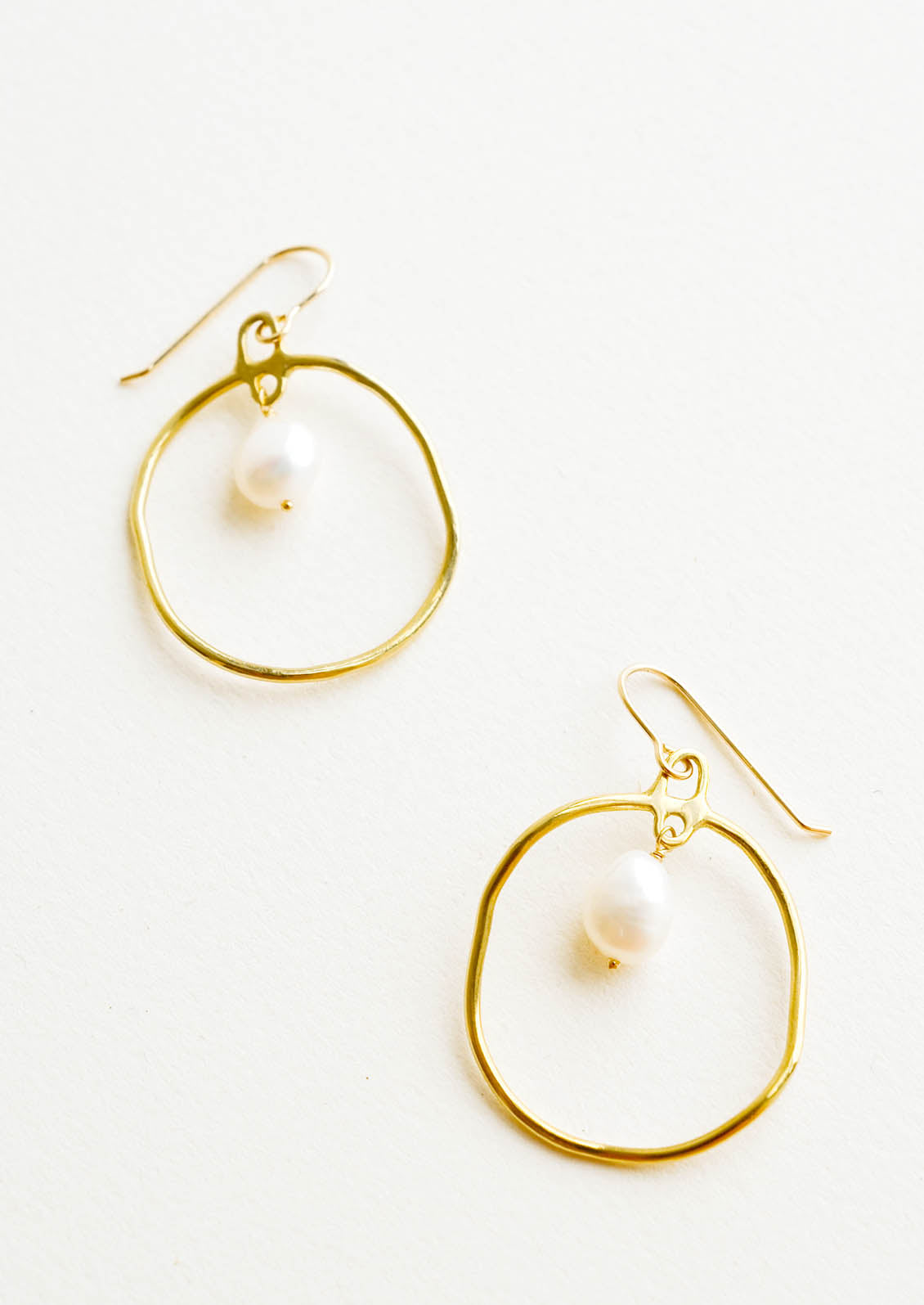 Circular drop earrings in gold with a small pearl dangling within.